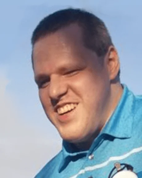 Man smiling with cropped brown hair in a light-blue polo holding his cane.