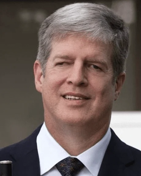 Middle-aged man smiling with grey hair, in a dark suit is holding a white cane