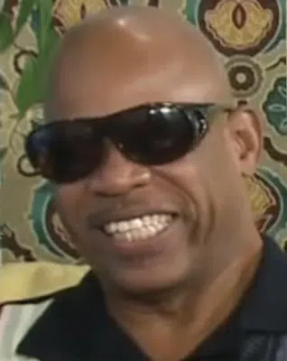 Bold black man with a dark sunglasses and a big toothy smile.